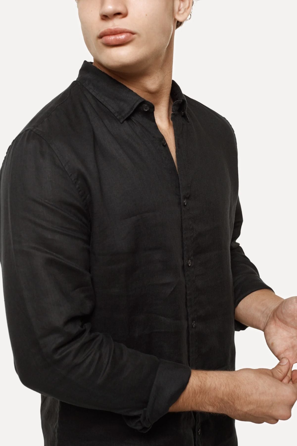 A person wears the Industrie The Tennyson Linen Shirt with rolled-up sleeves against a plain backdrop. Their head is slightly turned, showcasing its classic style, and a hand appears in front, highlighting the shirt's relaxed fit.