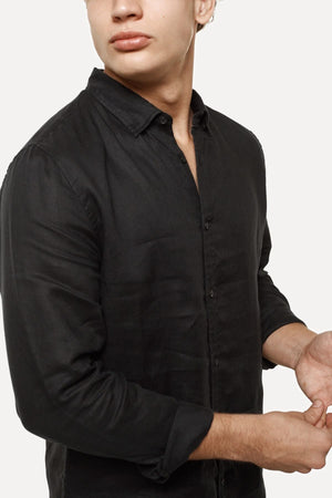 A person wears the Industrie The Tennyson Linen Shirt with rolled-up sleeves against a plain backdrop. Their head is slightly turned, showcasing its classic style, and a hand appears in front, highlighting the shirt's relaxed fit.
