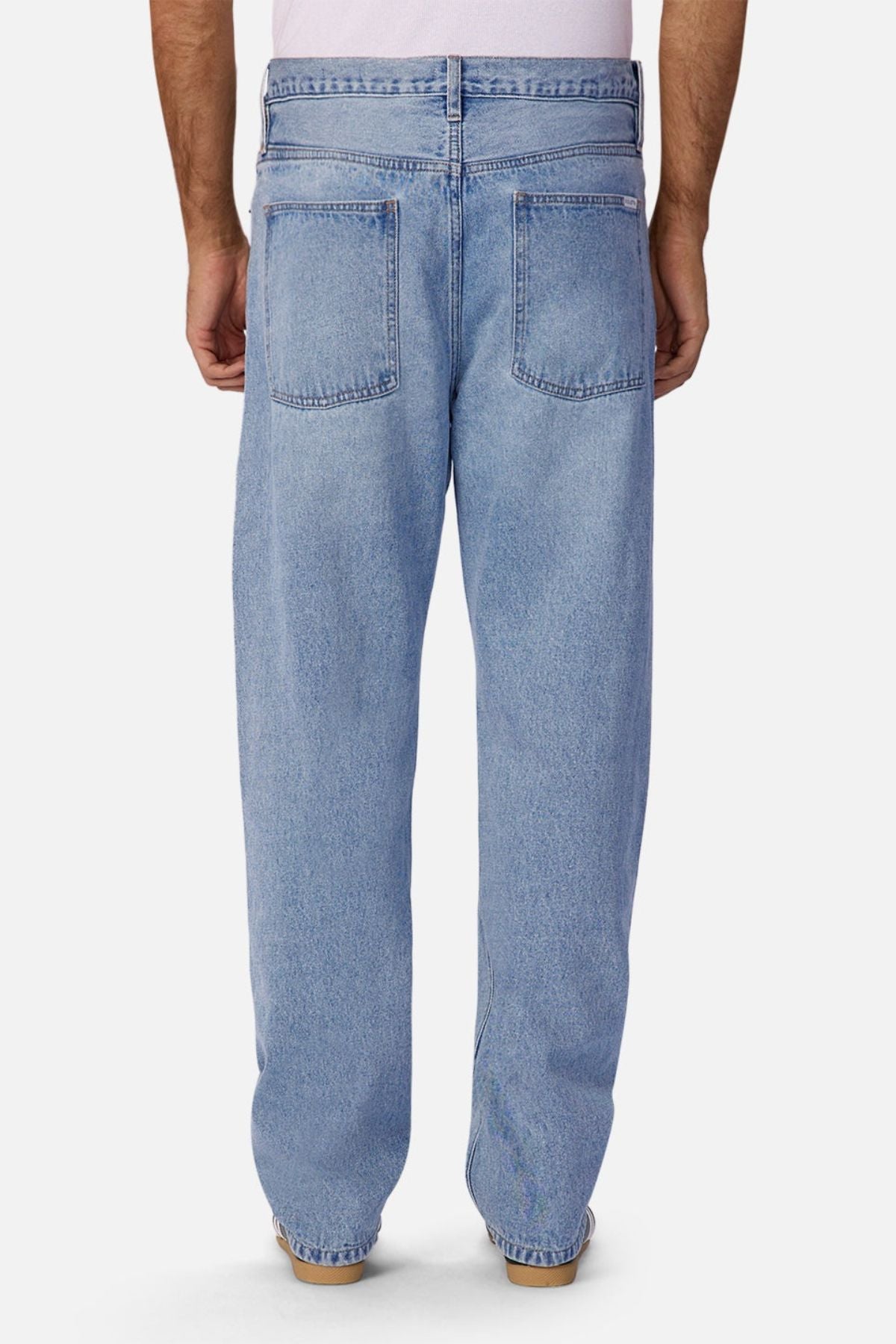 A person is seen from the back wearing Industrie The 90's Jean in light blue, vintage washed 100% cotton denim with relaxed straight legs and two large back pockets, paired with brown shoes and arms at their sides.