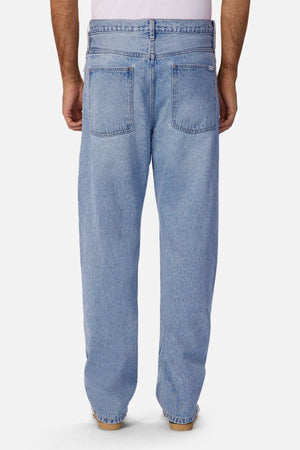 A person is seen from the back wearing Industrie The 90's Jean in light blue, vintage washed 100% cotton denim with relaxed straight legs and two large back pockets, paired with brown shoes and arms at their sides.