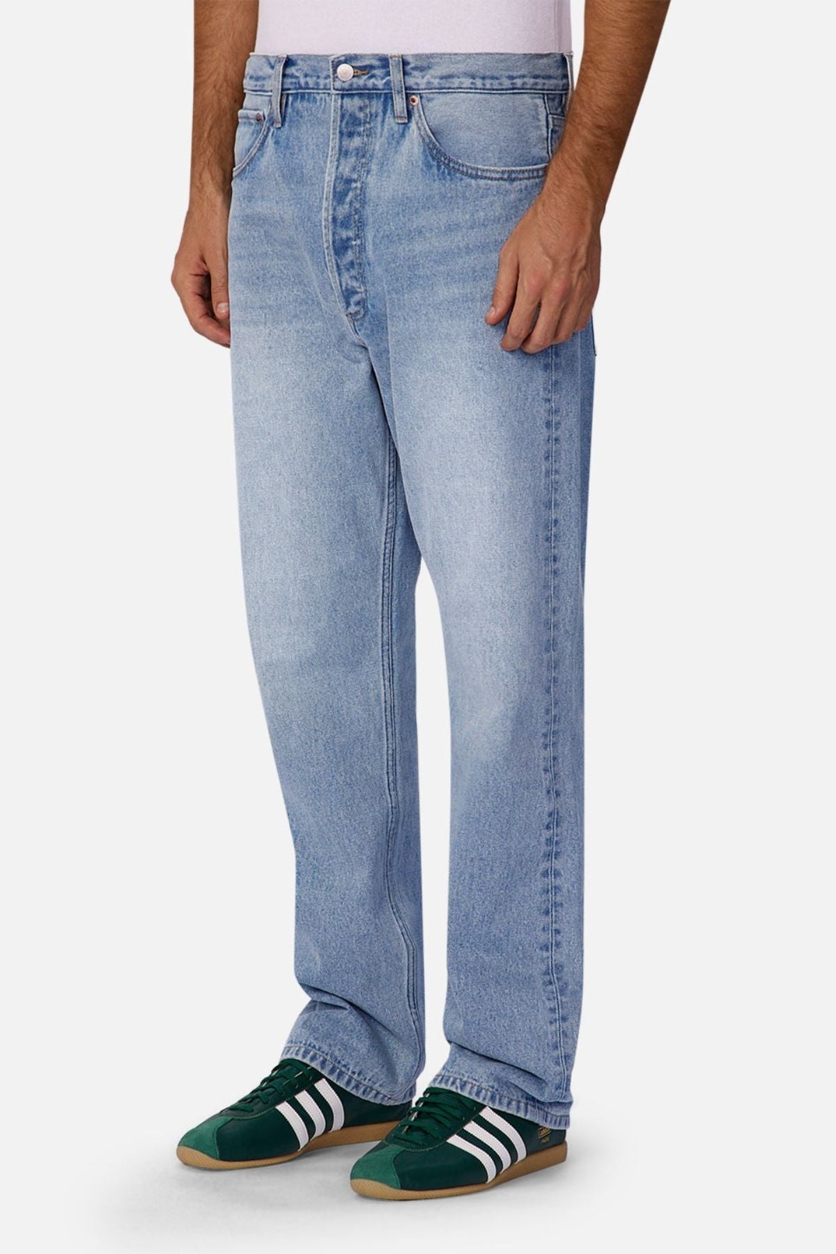 Someone wearing Industrie The 90's Jean, a white shirt, and green Adidas sneakers with white stripes stands against a plain white background.
