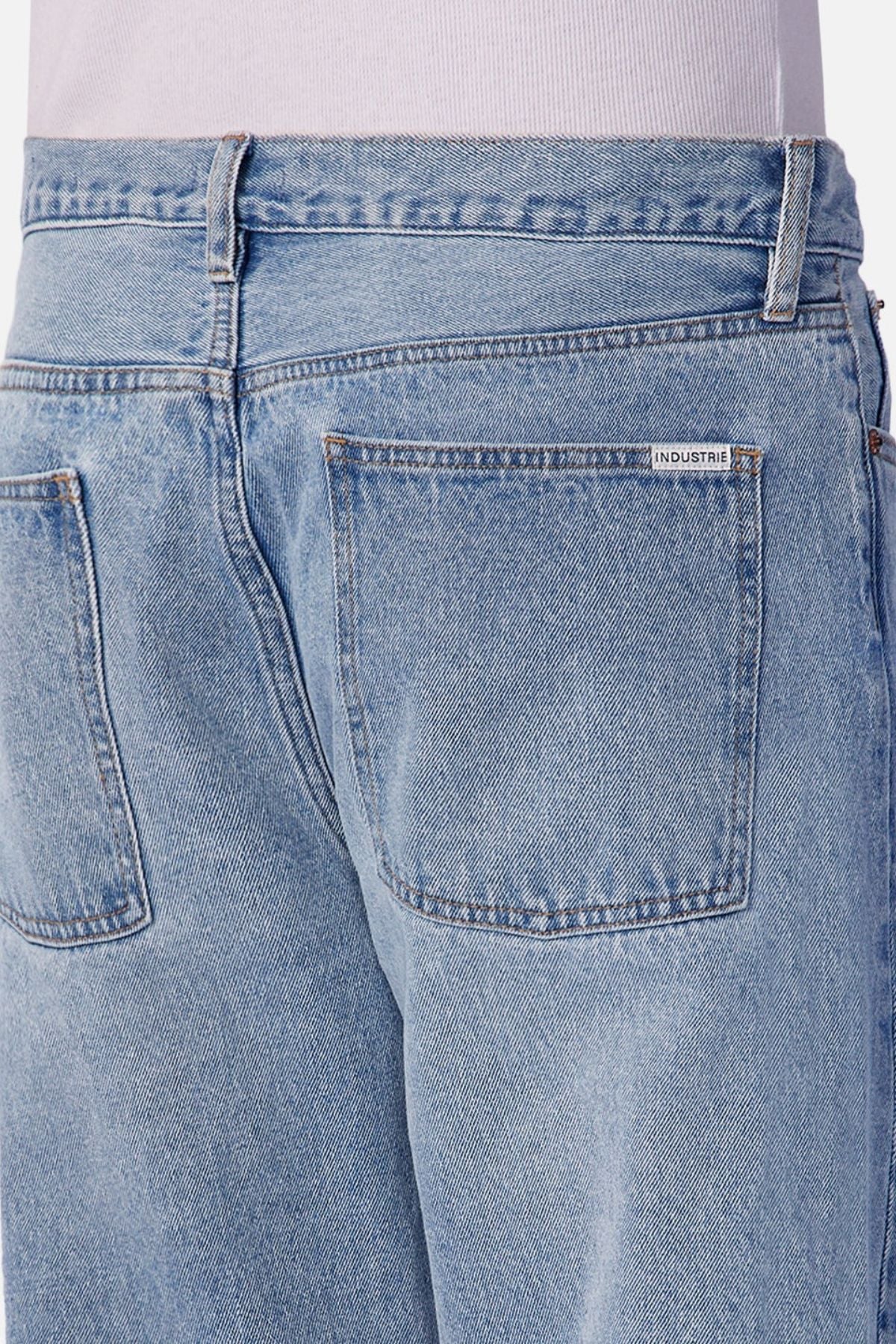 Close-up of the back of a person wearing Industrie The 90's Jean—vintage washed, light blue relaxed straight leg jeans with two back pockets, a small white INDUSTRIE label above the right pocket, and a light shirt visible at the waist.