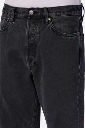 Close-up of a person wearing Industrie The 90's Jean, featuring high-waisted black vintage washed denim, front pockets, metal button, detailed stitching, and a relaxed straight leg cut for an authentic 90's vibe.