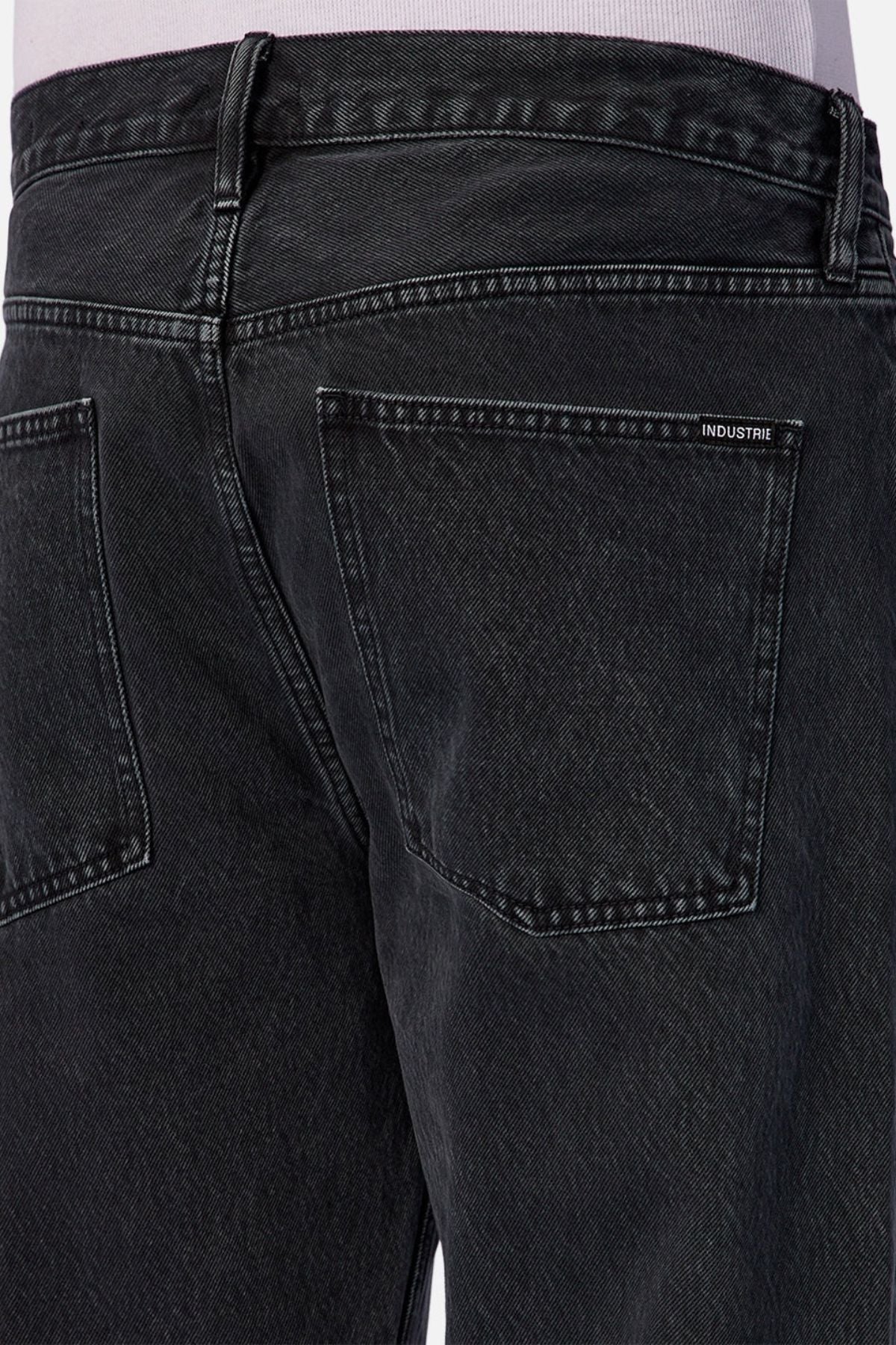 Close-up of the back of a person wearing Industrie The 90’s Jean in vintage washed denim—black, relaxed straight leg with two back pockets and a small "INDUSTRIE" label above the right pocket.