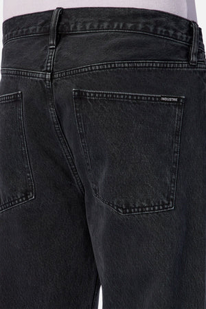 Close-up of the back of a person wearing Industrie The 90’s Jean in vintage washed denim—black, relaxed straight leg with two back pockets and a small "INDUSTRIE" label above the right pocket.