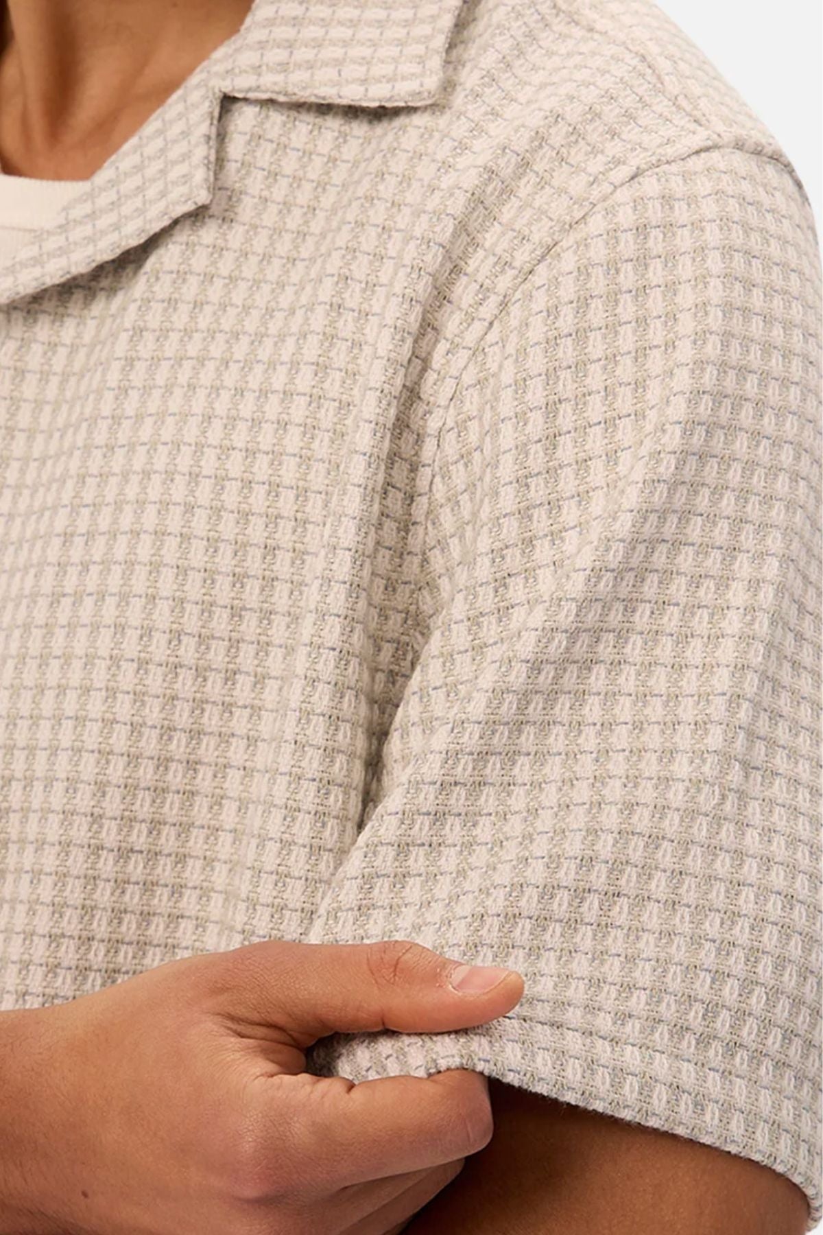 A close-up of a person wearing the Industrie The Almeria Short Sleeve Shirt in light gray with a waffle texture, gently pulling on the sleeve with their right hand.