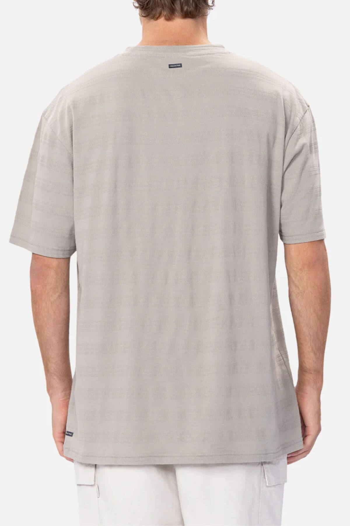 A person is seen from the back wearing the Industrie The Anderson Textured Stripe Tee in light grey with subtle horizontal stripes and a small logo tag near the neckline, paired with light shorts against a plain white background.