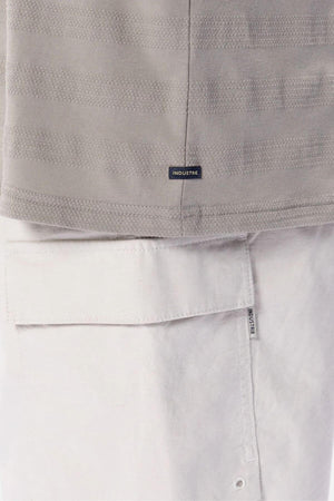 Close-up of a person wearing the Industrie The Anderson Textured Stripe Tee in light grey, paired with white pants featuring a large pocket and an Industrie label near the seam.
