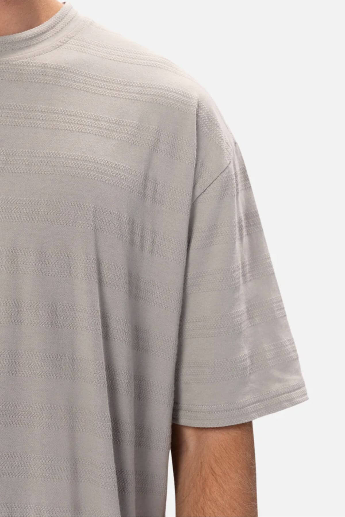 Close-up of a person wearing the Industrie The Anderson Textured Stripe Tee in light grey, featuring subtle horizontal stripes, showing the upper chest, shoulder, and part of the arm against a white background.