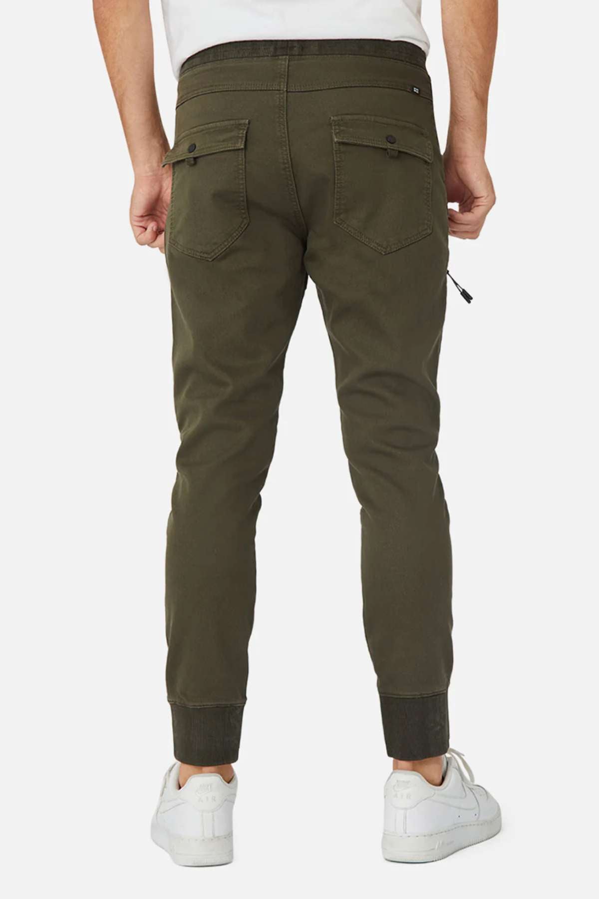 A person is seen from behind wearing olive green Industrie The Armoured Drifter Pant joggers with buttoned back pockets and ribbed cuffs, paired with white sneakers—ideal for the modern adventurer.