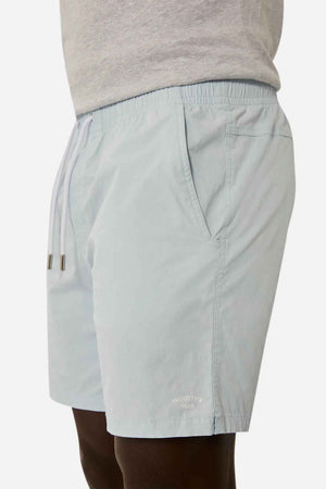 A person is seen in light blue Industrie The Bahama Angler Shorts, complete with an elastic drawcord waist and side pockets, showcasing the "Industrie 1999" branding near the hem. They complement their outfit with a gray shirt.