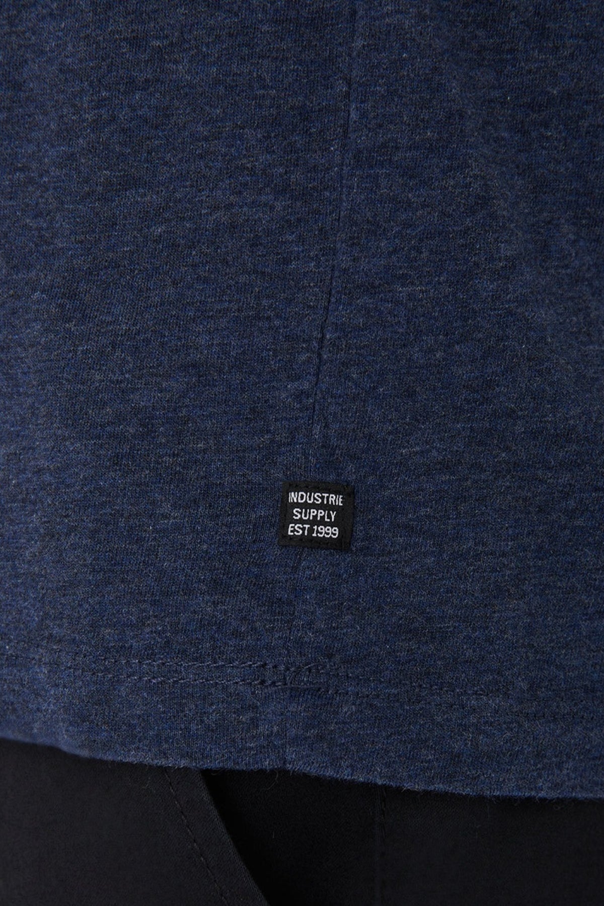 Close-up of Industrie The Basic Crew Tee in dark blue, 100% cotton, with a small black "INDUSTRIE SUPPLY EST 1999" label at the hem. This classic-fit shirt is shown paired with black pants.