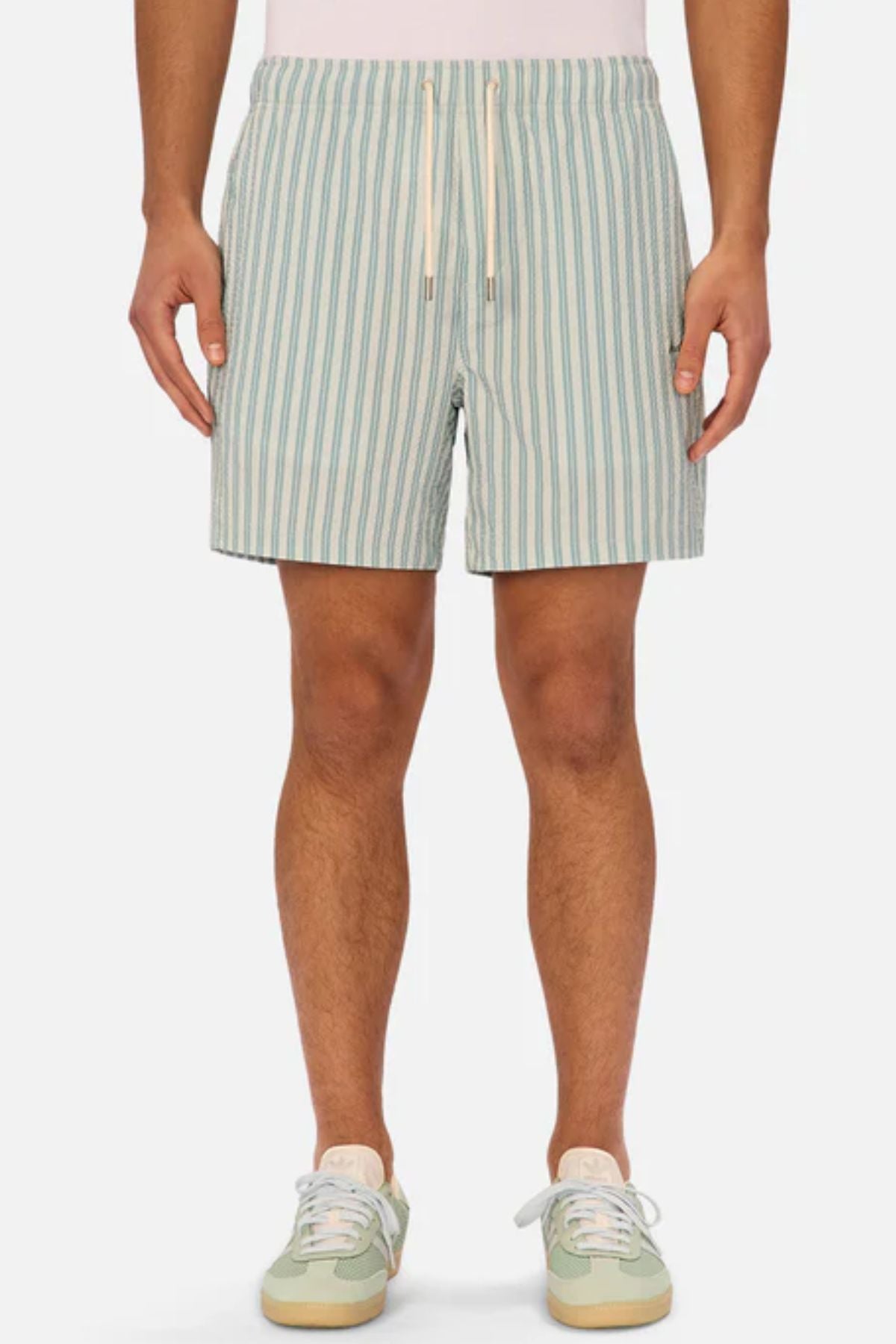 A person wearing Industrie The Berkeley Swim Short in light blue and white vertical stripes with a drawstring waistband and matching sneakers, standing forward against a plain background—highlighting stylish men's swimwear.