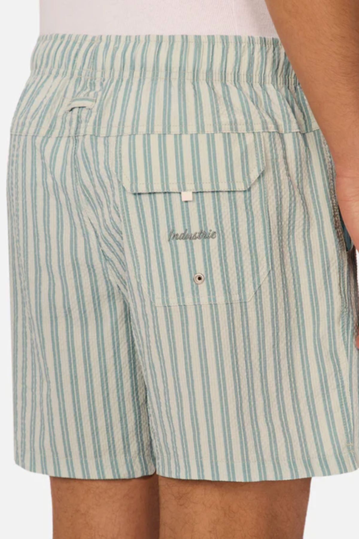 A person wearing light blue and white vertically striped Industrie The Berkeley Swim Short featuring a back pocket with a flap, button, and "malaurie" embroidered above it, making it a standout in men's swimwear.