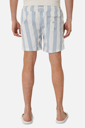 A person stands facing away, wearing Industrie The Beverly Bahama Short in light blue and white vertical stripes with white flip-flops. Shorts are made from breathable fabric. Background is plain white.