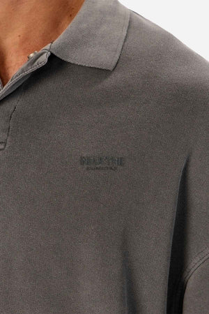Close-up of a person wearing the Industrie The Burbank Polo Track—a gray, premium polo shirt with subtle chest embroidery. Only the neck, shoulder, and upper chest are visible.