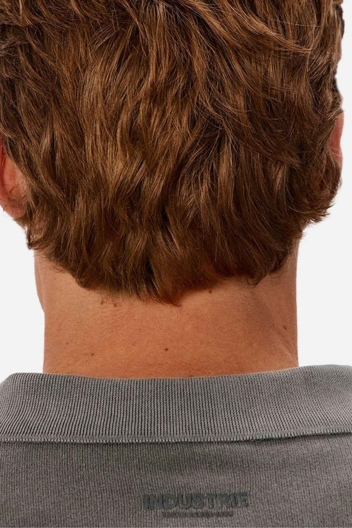 The image features the back of a person with short, wavy brown hair wearing a gray Industrie The Burbank Polo Track shirt against a plain white background.