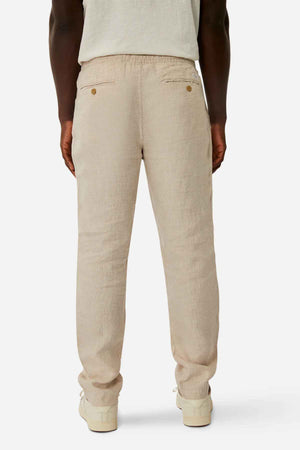 A person is seen from the back wearing Industrie The Capri Linen Pant in light beige, wide-leg fit with two buttoned back pockets, paired with a white shirt and off-white shoes against a plain white background, exuding a summer vibe.