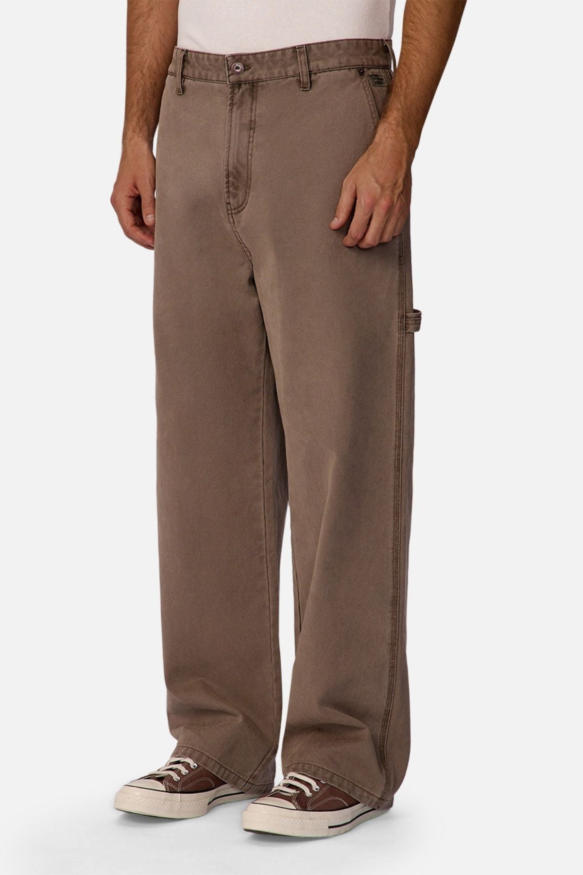 A person wearing the Industrie The Carolina Carpenter Pant in loose-fitting brown cotton, paired with a white shirt and brown sneakers, shown from shoulders to feet against a plain white background.