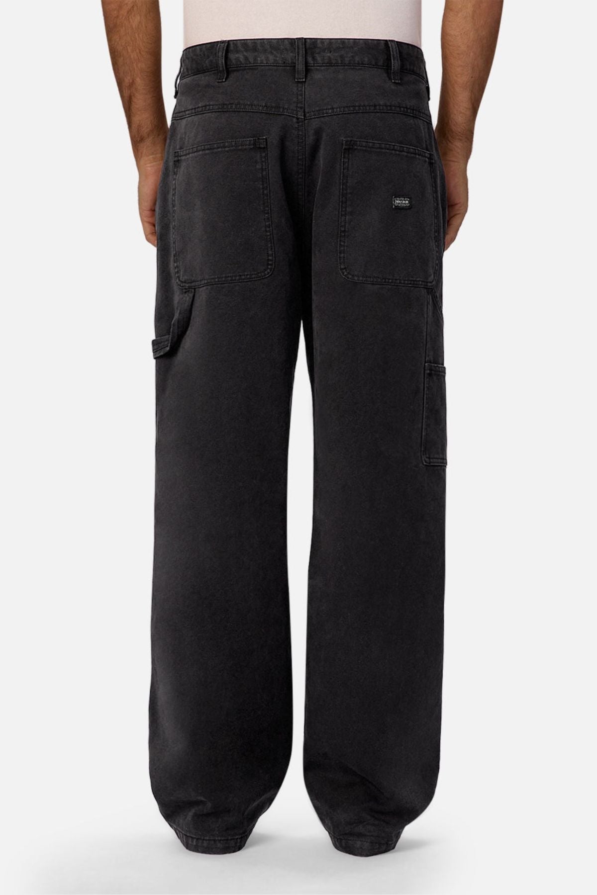 A person is shown from the waist down, wearing Industrie The Carolina Carpenter Pant in black with large back and side pockets, standing against a plain, light background.