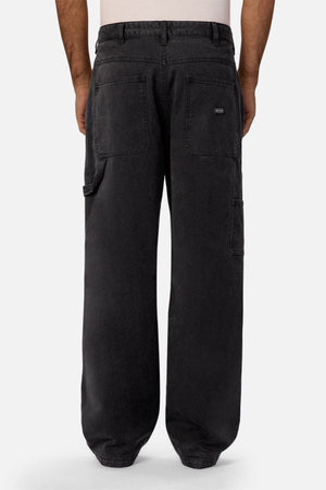A person is shown from the waist down, wearing Industrie The Carolina Carpenter Pant in black with large back and side pockets, standing against a plain, light background.