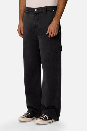 Someone wearing Industrie The Carolina Carpenter Pant in a relaxed fit, paired with black low-top sneakers with white soles and laces, stood against a plain light background. Only the lower body is shown.