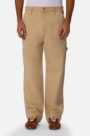 A person wears Industrie The Carolina Carpenter Pant, featuring loose-fitting, durable cotton and utility pockets, paired with brown shoes against a plain white background.