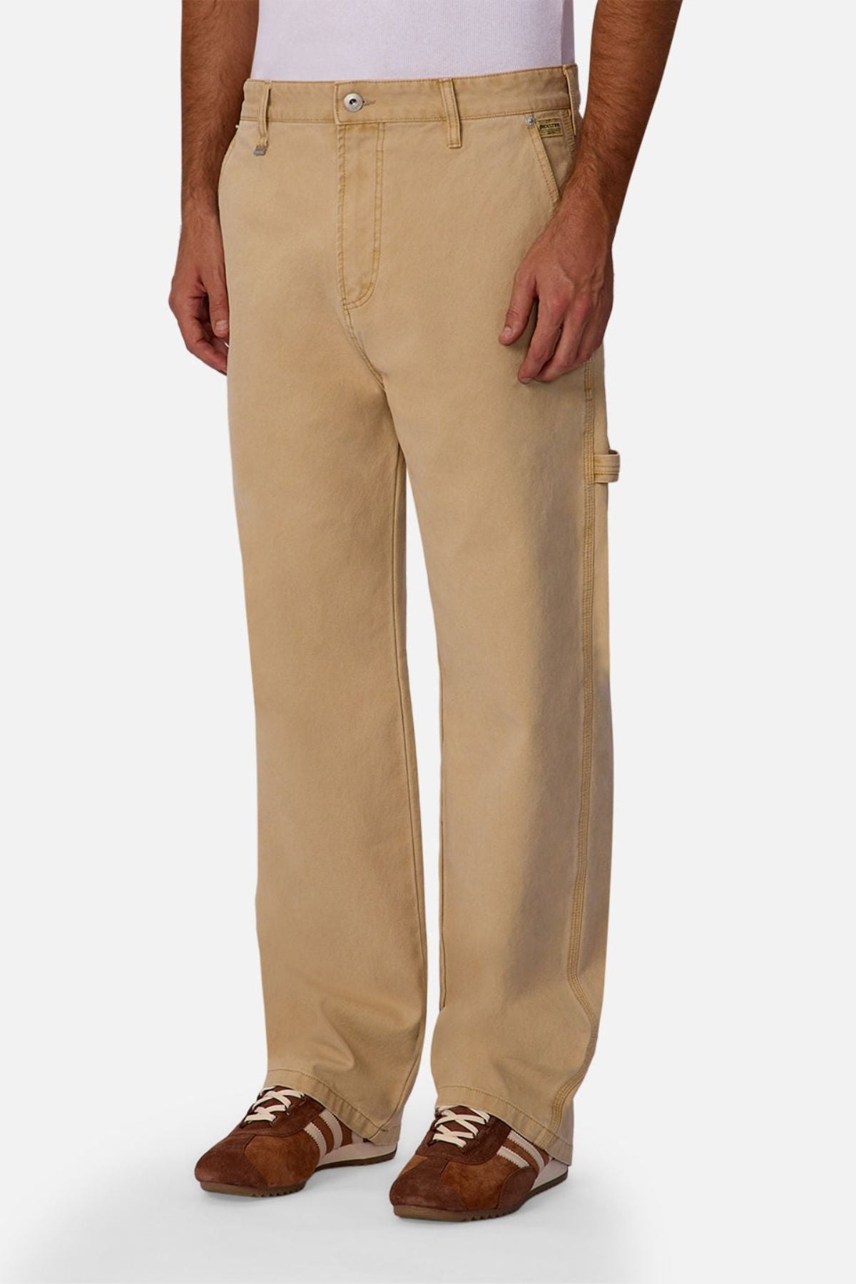 A person wearing Industrie The Carolina Carpenter Pant, featuring durable cotton, relaxed fit, and a side utility loop, along with brown sneakers with white accents, stands against a plain white background.