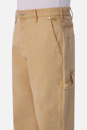A close-up of Industrie The Carolina Carpenter Pant in durable cotton, featuring side pockets, a hammer loop, visible stitching, and a brand label above the right pocket as worn by a model.