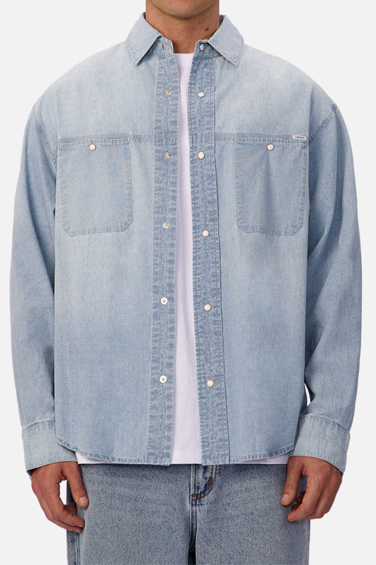 A person wearing the Industrie The Chambray Nebraska Long Sleeve Shirt over a white tee with matching light blue jeans, shown from shoulders to hips against a plain background—a timeless men's workwear look.