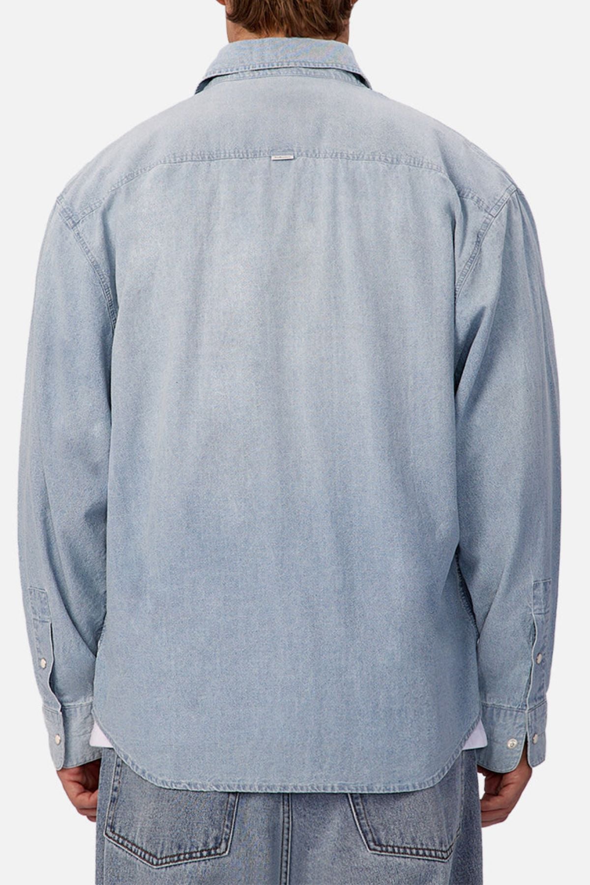 A person is seen from behind wearing the Industrie The Chambray Nebraska Long Sleeve Shirt with buttoned cuffs and a straight hem, paired with denim jeans against a plain light background, showcasing classic men's workwear style.
