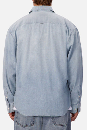 A person is seen from behind wearing the Industrie The Chambray Nebraska Long Sleeve Shirt with buttoned cuffs and a straight hem, paired with denim jeans against a plain light background, showcasing classic men's workwear style.