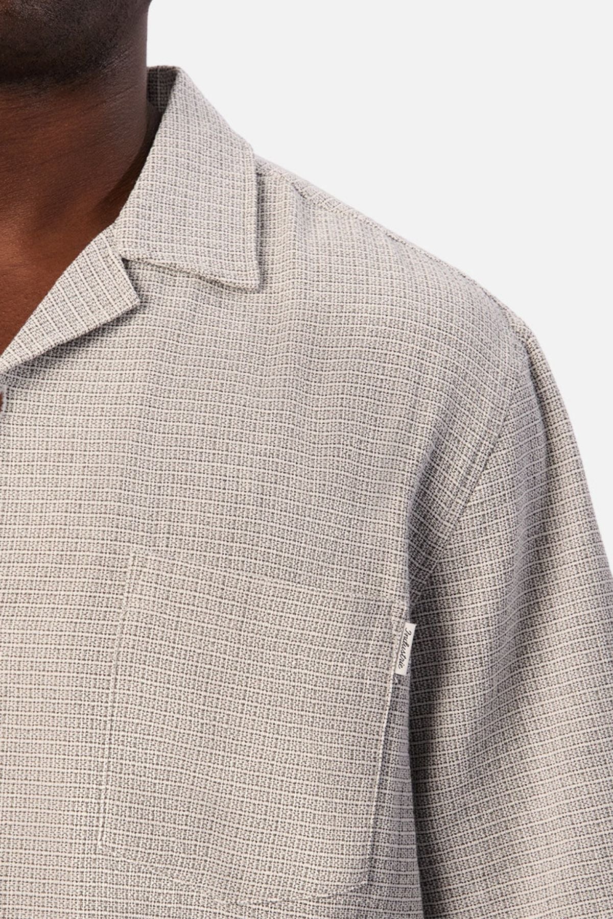 Close-up of a person wearing the Industrie The Check Marbella Short Sleeve Shirt in light gray textured fabric, featuring a collar and chest pocket. The top button is left undone, giving this casual shirt a relaxed feel, with only part of the person’s face and upper torso visible.