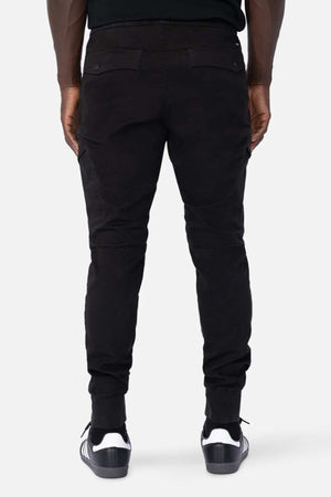 Rear view of a person immersed in their active lifestyle, wearing stylish black Industrie The Defender Combat Pants and sleek black sneakers with white soles, standing confidently against a neutral background.