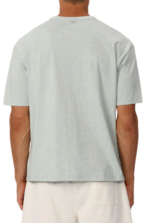 A person is shown from behind against a white background, wearing the Industrie The Del Sur Tee in light gray heavyweight fabric and off-white shorts.