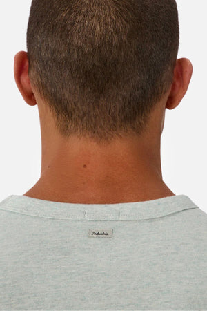 A close-up of the back of a person's head shows short brown hair and a light gray Industrie The Del Sur Tee with a small "Industrie" label on the collar. The tee is made from heavyweight fabric, set against a plain white background.