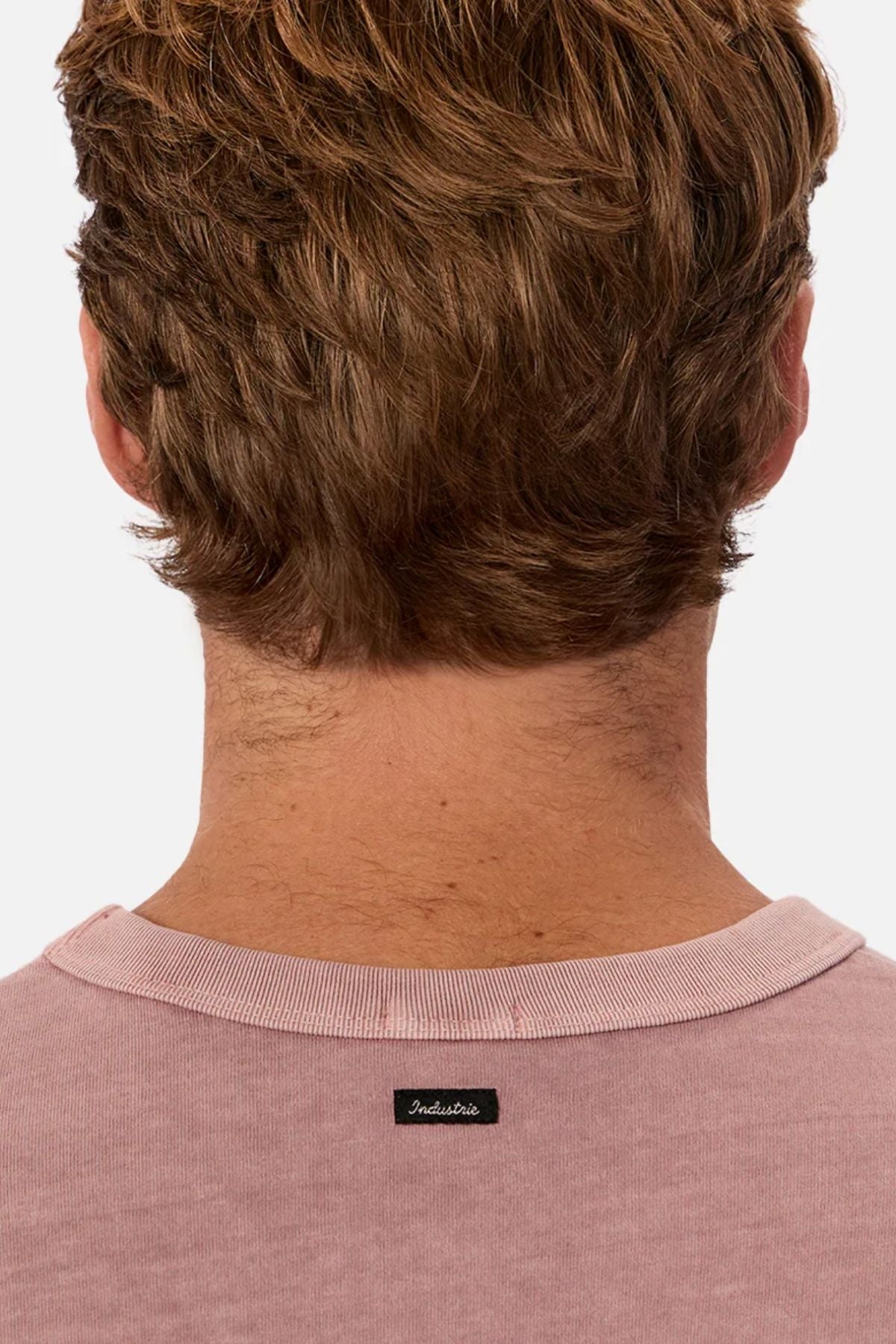 A close-up shows the back of a person's head and neck with short brown hair, wearing the pink Industrie The Del Sur Tee made from heavyweight fabric, featuring a small black Industrie label.