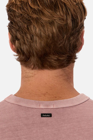 A close-up shows the back of a person's head and neck with short brown hair, wearing the pink Industrie The Del Sur Tee made from heavyweight fabric, featuring a small black Industrie label.