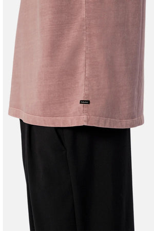 Close-up of a person in the Industrie The Del Sur Tee, dusty pink, with black pants. The image highlights the tee’s heavyweight fabric and a subtle black label near the hem.
