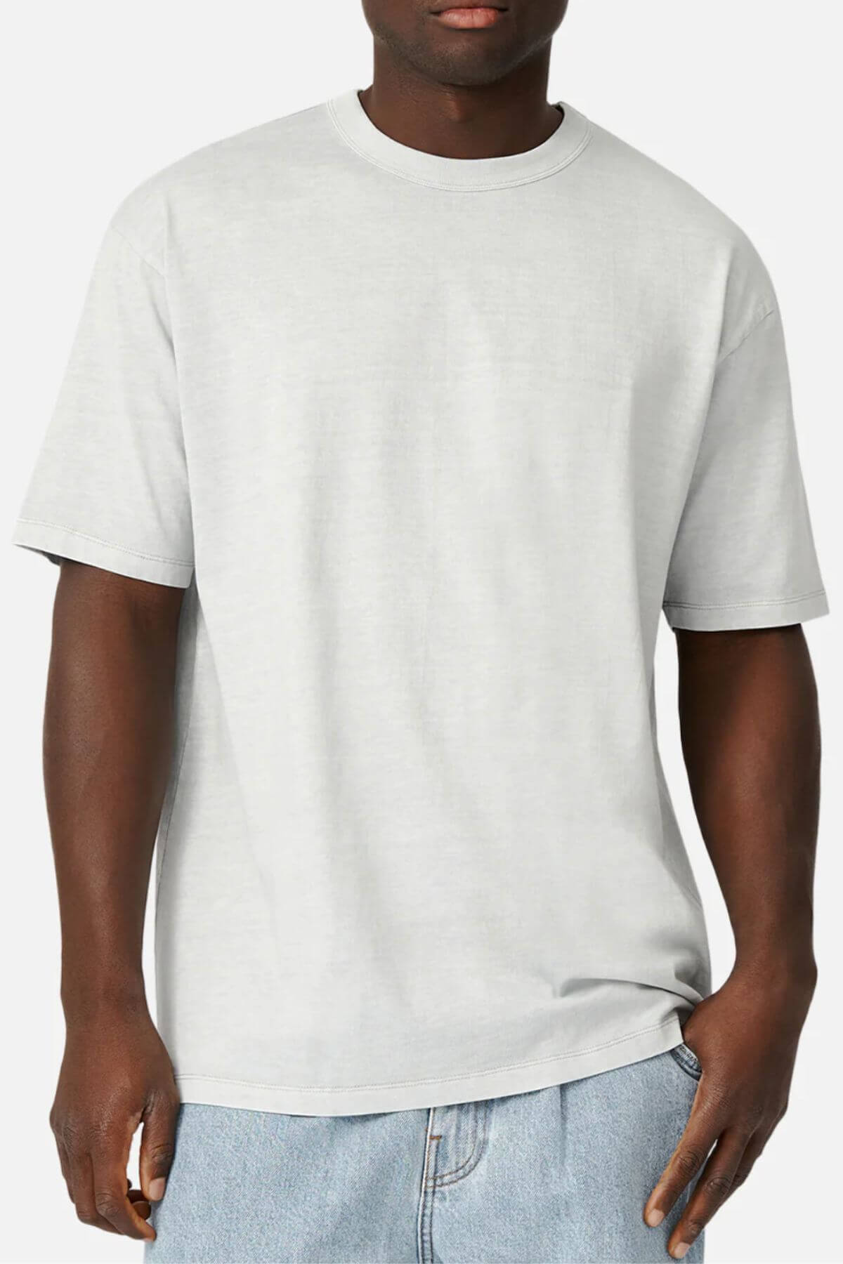 A person is wearing an Industrie The Del Sur Tee with an oversized fit, made from 100% cotton, alongside light blue jeans against a neutral backdrop. The T-shirt has short sleeves and a relaxed style, with the person's hand partially tucked into the jeans pocket.