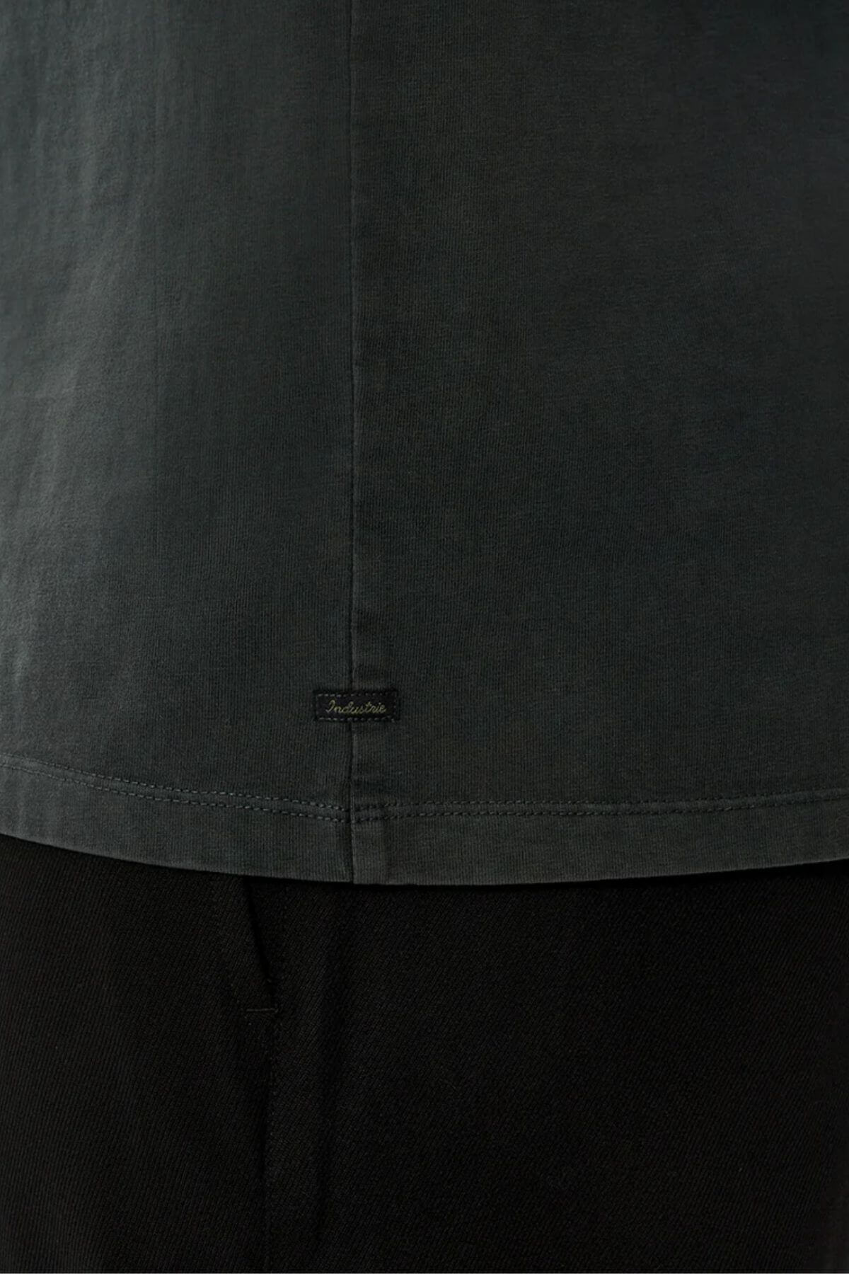 Close-up of the lower back of the Industrie The Del Sur Tee, featuring a small black rectangular label near the hem. Made from smooth 100% cotton with visible stitching for a premium look, paired here with black pants.