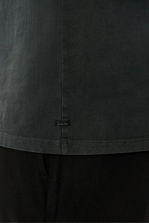 Close-up of the lower back of the Industrie The Del Sur Tee, featuring a small black rectangular label near the hem. Made from smooth 100% cotton with visible stitching for a premium look, paired here with black pants.