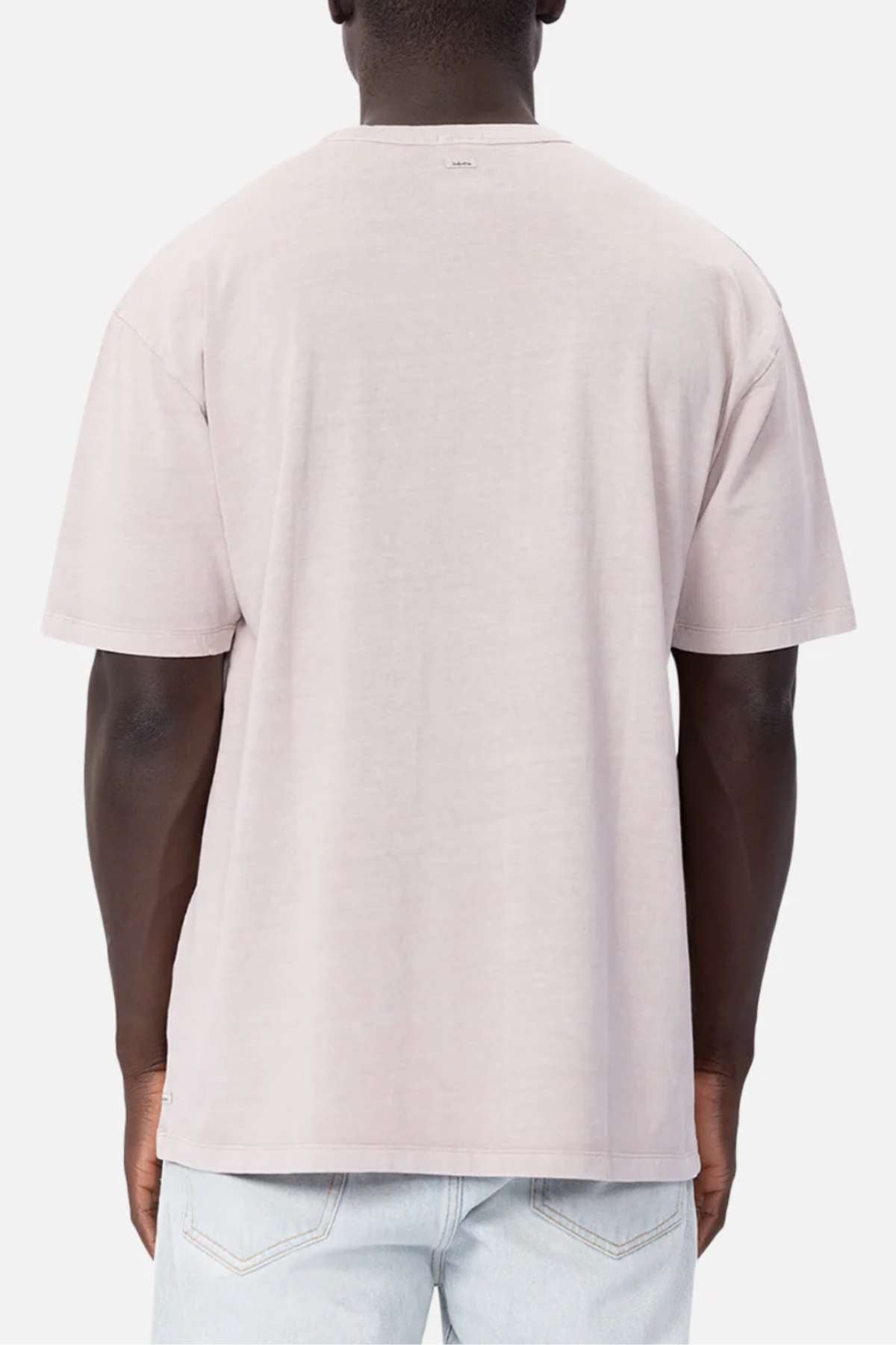 A person with dark skin is shown from the back, wearing an Industrie The Del Sur Tee, a light grey, short-sleeve t-shirt made of 100% cotton. This comfortable tee features an oversized fit for extra comfort and is plain without any visible logos or designs. They are also wearing light blue jeans against a plain white background.