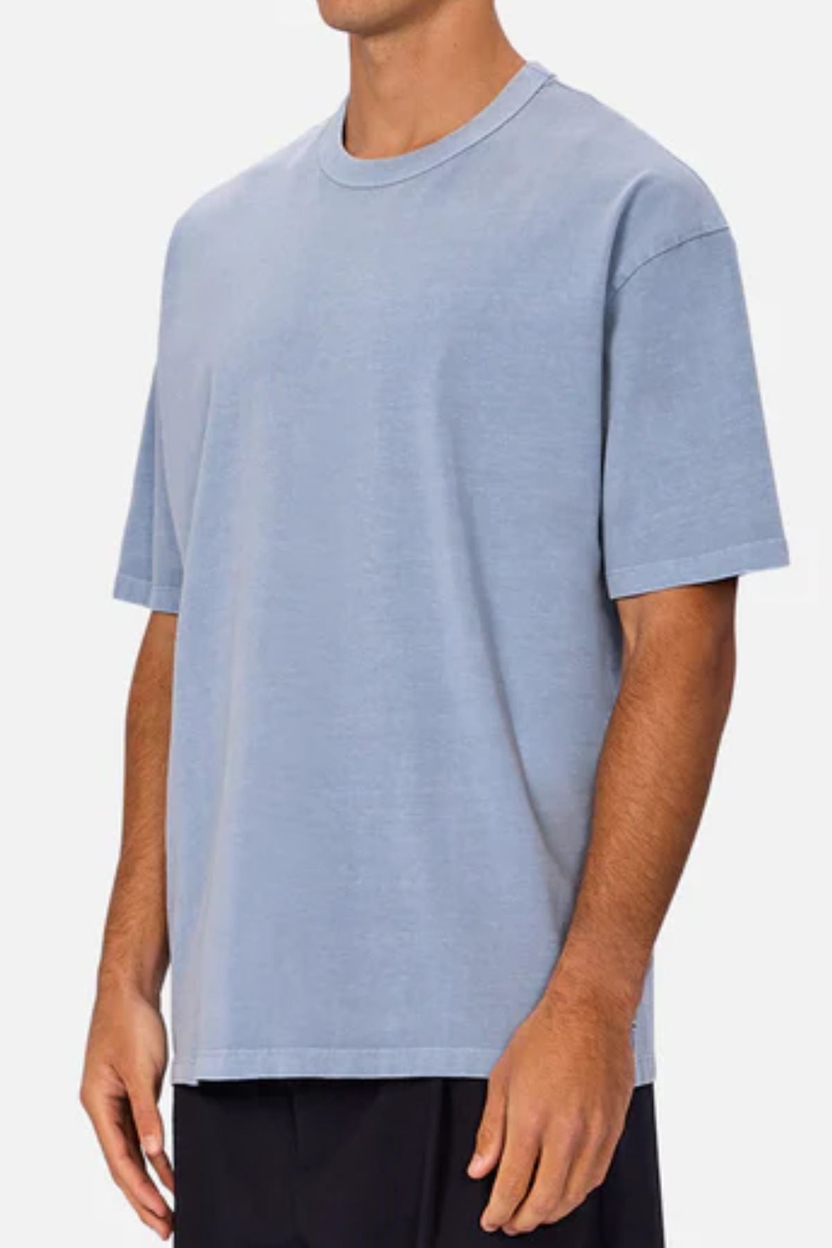 Someone wears an oversized Industrie The Del Sur Tee in light blue heavyweight fabric with black pants, standing against a plain light background. The top of their head is not fully visible in the image.