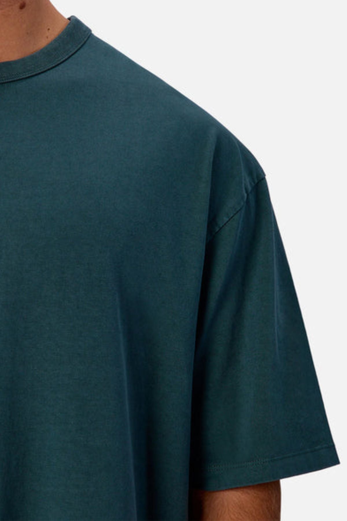 A close-up of a person wearing the Industrie The Del Sur Tee in teal, featuring an oversized fit and heavyweight cotton fabric, with the upper torso and part of one arm visible against a plain light background.