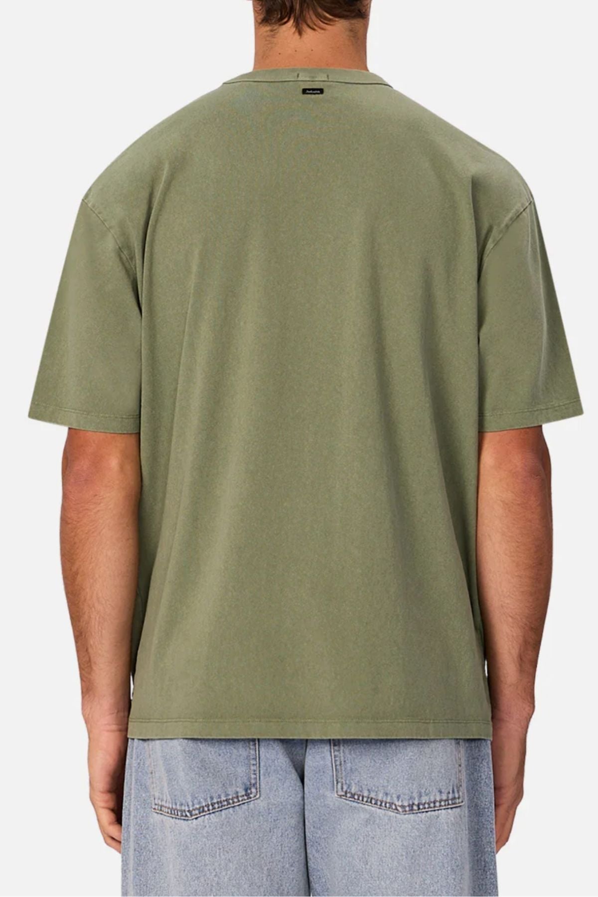 A person is shown from behind in an oversized olive green Industrie The Del Sur Tee made from heavyweight fabric, paired with light blue denim shorts, set against a plain white background.