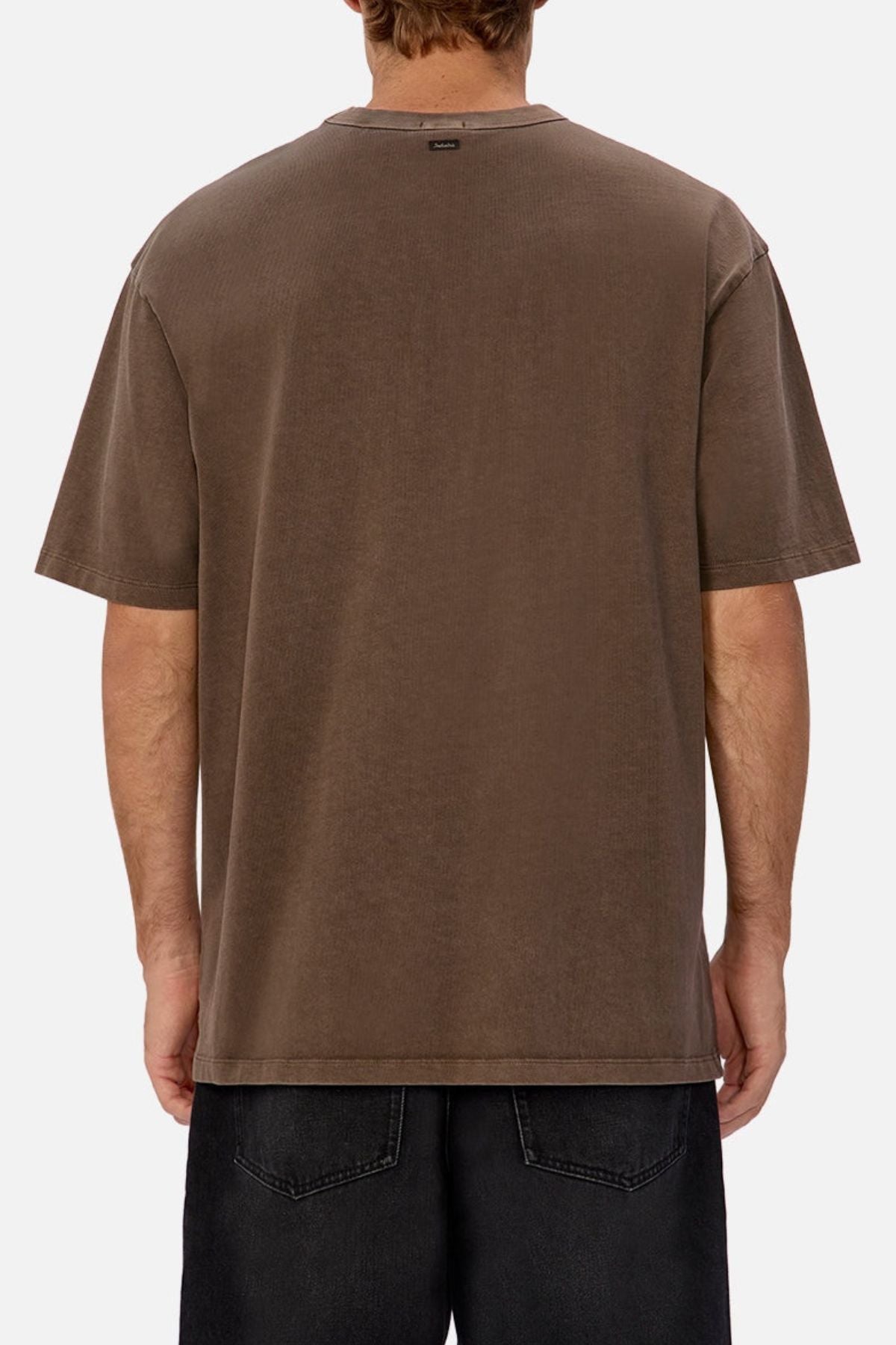 A person faces away from the camera, wearing an oversized Industrie The Del Sur Tee in brown with black denim shorts. The plain white background highlights the tee's heavyweight cotton fabric and relaxed, casual style.