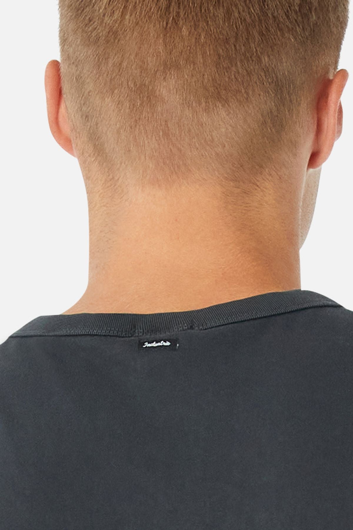 Close-up of the back of a person's head with short light brown hair, wearing the Industrie The Del Sur Tee. This black, oversized 100% cotton T-shirt features a small white label near the collar, shown against a plain white background.