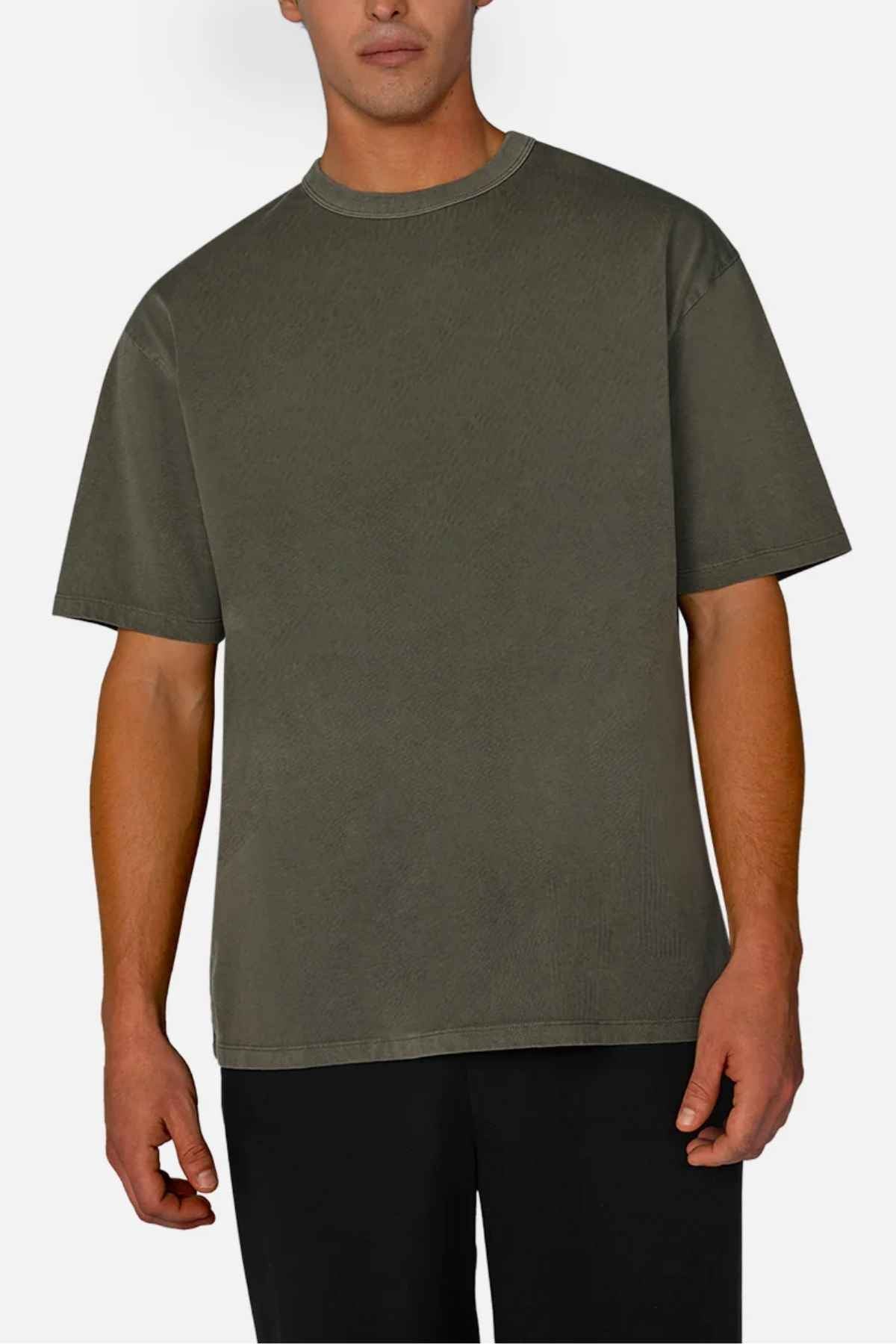 A person wearing the Industrie The Del Sur Tee, an oversized olive green acid wash t-shirt, stands against a light background paired with black pants. The relaxed fit with short sleeves enhances the casual vibe.