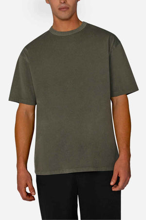 A person wearing the Industrie The Del Sur Tee, an oversized olive green acid wash t-shirt, stands against a light background paired with black pants. The relaxed fit with short sleeves enhances the casual vibe.